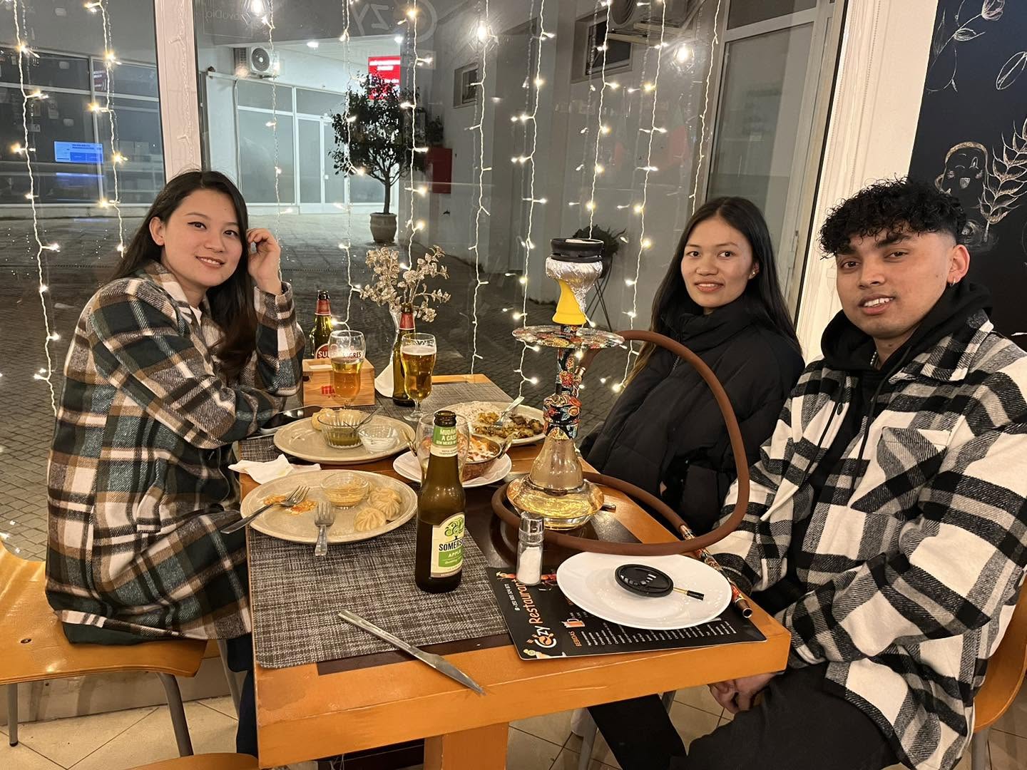 Three guests smiling around a table of momo and curries under warm fairy lights at Cozy Restaurant